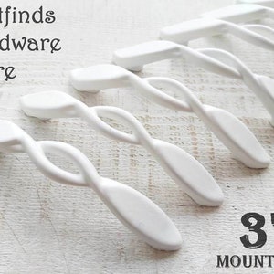 May include: White, twisted design cabinet pulls. The pulls are 7.6 cm in length and have a unique, modern shape. The text "firstfinds hardware store" is visible at the top left. The text "3" and "MOUNTING" are visible at the bottom right.
