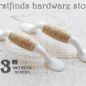 May include: Two white cabinet knobs with a 7.6 cm centre to centre spacing. The knobs are wrapped in natural twine.