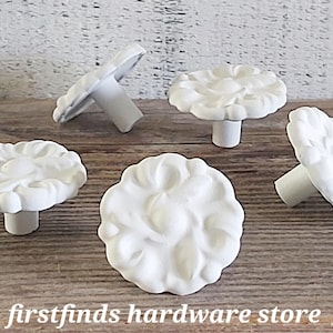 May include: Five white ceramic drawer knobs with a floral design. The knobs have a raised design and a smooth finish.