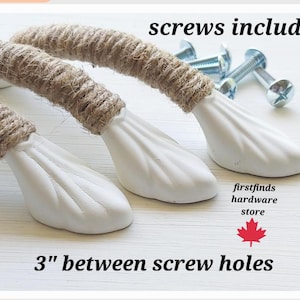May include: Three drawer pulls featuring white, shell-shaped metal ends and a centre wrapped in natural tan jute rope. The hardware includes silver-coloured metal screws. Text on the image reads: screws included, firstfinds hardware store, 3" between screw holes.