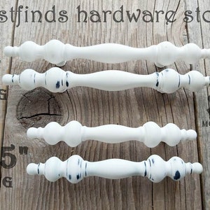 May include: Three white cabinet knobs with black accents. The knobs are 6 inches, 4.5 inches, and 3 inches long. The knobs are distressed and have a rustic look.