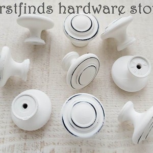 May include: White ceramic cabinet knobs with black trim. The knobs are round and have a small hole in the centre.