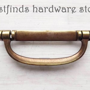 May include: A brass cabinet pull with a rectangular top and a curved bottom. The pull has a slightly aged finish.