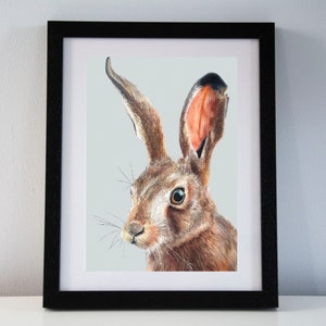 May include: A framed art print featuring a detailed illustration of a brown hare. The hare has long ears, detailed fur, and a focused gaze. The artwork is set against a light gray background and framed in a black frame, suitable for home decor.