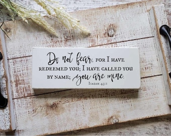 May include: A rectangular white wooden sign with black text that reads: Do not fear, FOR I HAVE REDEEMED YOU; I HAVE CALLED YOU BY NAME; you are mine. Isaiah 43:1. The sign is placed on a white distressed wooden tray with black metal handles.