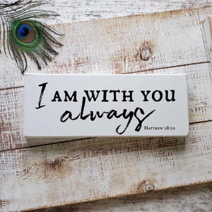 May include: A distressed white wooden tray with black handles and the text "I AM WITH YOU always Matthew 28:20" in black. A peacock feather with blue, green, and brown accents rests on the tray.