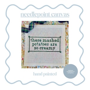 May include: A hand-painted needlepoint canvas with the text "these mashed potatoes are so creamy" in a green frame. The canvas is white with a green and white plaid ribbon and the words "needlepoint canvas" at the top.