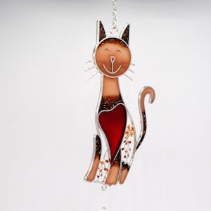 May include: A stained glass cat wind chime with a red heart and orange flowers. The cat is brown and has a black outline. The chime has a clear glass ball with red and orange flowers.