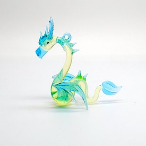 May include: A glass dragon figurine with a light blue and green color scheme. The dragon has a long neck, wings, and a tail.