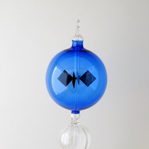May include: A decorative glass object with a blue orb and a clear, teardrop-shaped base. The blue orb has a black design inside. The object is likely a decorative piece or a scientific instrument.