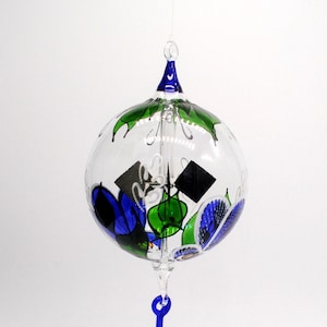 May include: A glass wind chime with a blue and green floral design. The chime is round and has a blue glass drop at the bottom.