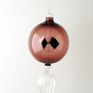 May include: A glass Christmas ornament with a deep purple hue and a clear glass teardrop-shaped finial. The ornament has a reflective surface.
