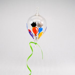 May include: A glass ornament shaped like a hot air balloon with a green ribbon. The balloon is filled with colourful balloons, including red, yellow, blue, and purple.