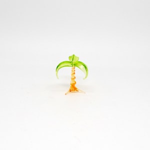 Peut inclure: Une petite figurine d'arbre en verre en forme de palmier avec des feuilles vertes et un tronc orange.