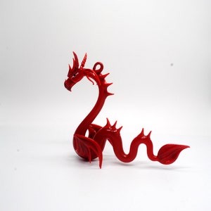 May include: A red glass dragon figurine with a curled tail and wings. The dragon has a detailed face with sharp teeth and horns.