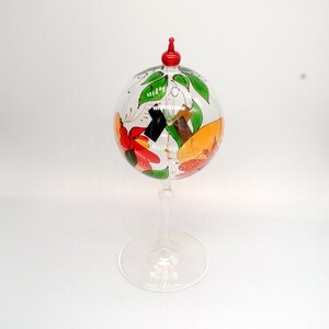 May include: A clear glass dome with a red top and a painted floral design. The dome sits on a clear glass pedestal.