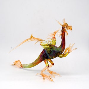 May include: A glass dragon figurine with iridescent wings and a multi-coloured body. The dragon is standing on its hind legs with its wings spread out.