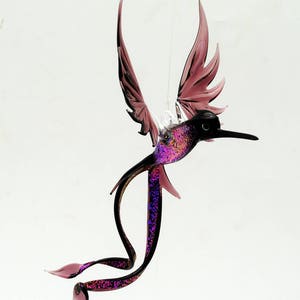 May include: A glass hummingbird ornament with iridescent purple and black wings. The hummingbird is in flight with its tail curled.