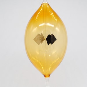 May include: A glass ornament shaped like a teardrop with a gold and black geometric design inside.