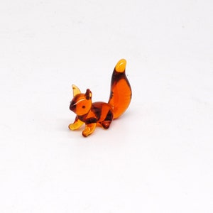 May include: A small glass squirrel figurine with a brown amber color. The squirrel is standing on all fours with its tail curled up behind it.