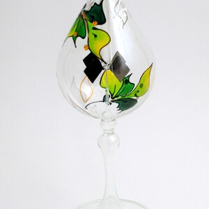 May include: A clear glass vase with a teardrop-shaped body and a tall stem. The vase is decorated with painted green and yellow butterflies.