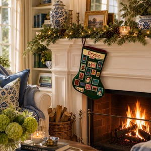 May include: A dark green Christmas stocking featuring a grid of embroidered postage stamp designs with holiday motifs, including a nutcracker, Santa, and snowman. The top cuff is cream-colored with the name Bryson embroidered in red text.
