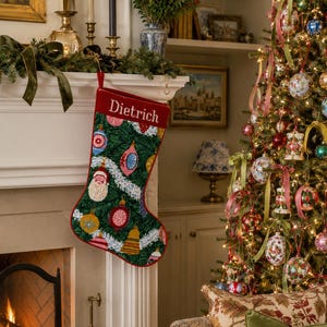Könnte beinhalten: Ein Weihnachtsstrumpf mit dunkelgrünem Hintergrund und einem Muster aus bunten, vintage-artigen Ornamenten sowie weißer Lamettagirlande. Der obere Rand ist einfarbig rot und trägt den Namen Dietrich in weißer Schreibschrift.