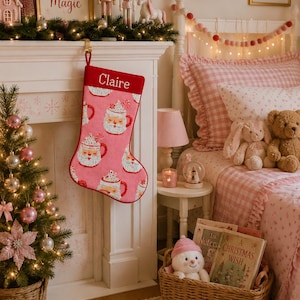 Puede incluir: Un calcetín navideño rosa con un patrón repetitivo de caras de Papá Noel en tazas con nata montada y bastones de caramelo. El borde superior es de color rosa oscuro con el nombre Claire bordado en letras blancas de estilo cursivo.