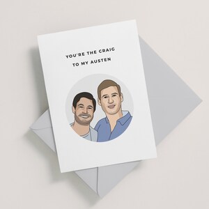 Op de afbeelding: Een kaart met een cartoonillustratie van twee mannen in een cirkel. De tekst op de kaart luidt "You're the Craig to my Austen."