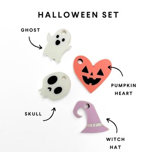 Op de afbeelding: Een set van vier Halloween-thema hangers, waaronder een spook, een schedel, een pompoenhart en een heksenhoed. De hangers zijn gemaakt van wit, zwart, oranje en paars acryl.
