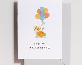 May include: A birthday card featuring a cartoon corgi dog with colorful balloons attached to its back. The card reads "Go Shorty It's Your Birthday".