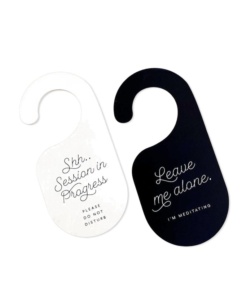 May include: Two door hangers with a hook top. The white hanger features black text reading Shh.. Session in Progress and PLEASE DO NOT DISTURB. The black hanger features white text reading Leave me alone. and I'M MEDITATING in a script font.