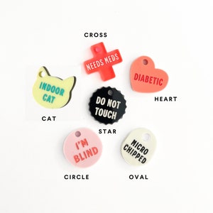 May include: Assortment of colorful pet ID tags in various shapes, including a cross, heart, star, circle, and oval. The tags feature text such as "Needs Meds", "Diabetic", "Do Not Touch", "I'm Blind", and "Micro Chipped".