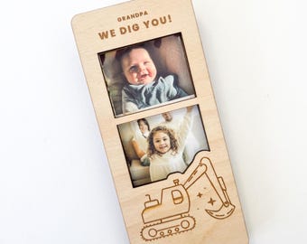 May include: Wooden photo frame with two picture slots and a decorative excavator design. The frame reads "GRANDPA WE DIG YOU!" and holds two photos of a baby and a young child.