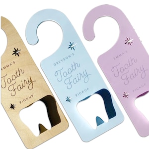 May include: Three door hangers in light wood, light blue, and light purple. Each features a cutout in the shape of a tooth at the bottom, two star icons, and the printed text "Tooth Fairy PICKUP" with a name above the phrase.