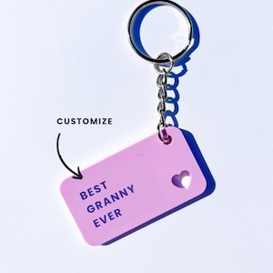 May include: A pink keychain with a silver key ring and chain. The keychain has a rectangular tag with the text "BEST GRANNY EVER" and a small heart cut out.