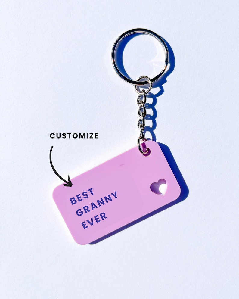 May include: A pink keychain with a silver key ring and chain. The keychain has a rectangular tag with the text "BEST GRANNY EVER" and a small heart cut out.