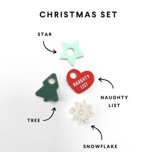 Op de afbeelding: Een kerstset van vijf ornamenten: een groene boom, een rood hart met de tekst "NAUGHTY LIST", een witte sneeuwvlok, een lichtblauwe ster en een witte sneeuwvlok.