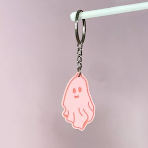 May include: A pink ghost keychain with a smiling face. The keychain is attached to a silver chain.