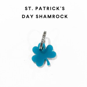 Op de afbeelding: Een turquoise klavertje vier-sleutelhanger met de tekst "ST. PATRICK'S DAY SHAMROCK" op een witte achtergrond.