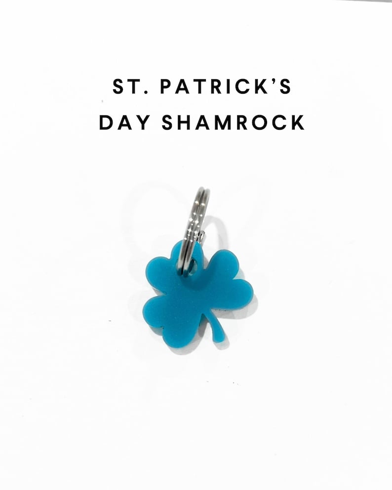 Op de afbeelding: Een turquoise klavertje vier-sleutelhanger met de tekst "ST. PATRICK'S DAY SHAMROCK" op een witte achtergrond.