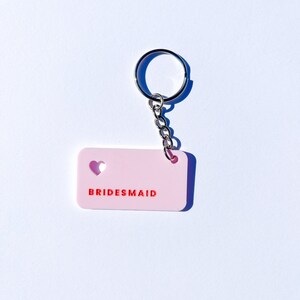 May include: Pink keychain with a heart cut-out and the word "BRIDESMAID" in red lettering.