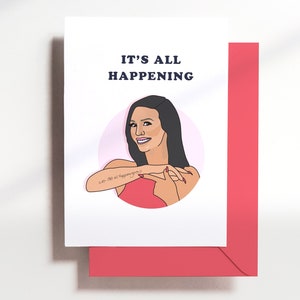 May include: A white card with a pink circle in the center. The circle contains a cartoon illustration of a woman with long black hair, wearing a red dress. The woman is smiling and making a gesture with her hands. The text "It's all happening" is printed in black above the circle.