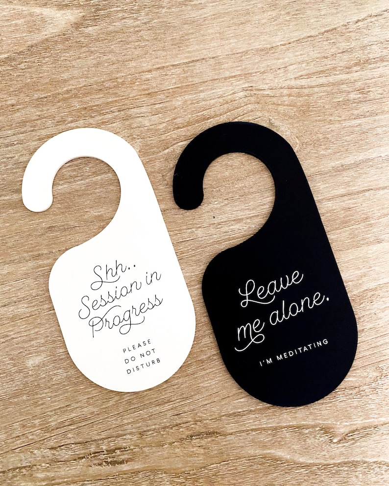 May include: Two door hangers with a hook top. One is white with black text reading Shh.. Session in Progress PLEASE DO NOT DISTURB. The other is black with white text reading Leave me alone. I'M MEDITATING. Both feature a rounded bottom shape.