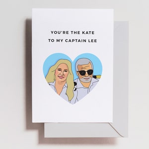 May include: A greeting card with a blue heart featuring a cartoon illustration of a woman and a man. The text on the card reads "You're the Kate to my Captain Lee."
