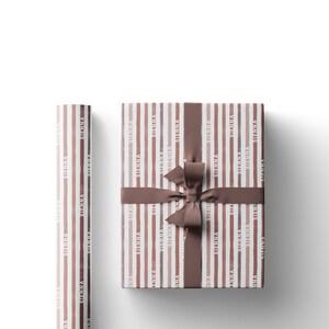 May include: Gift wrapping paper and a wrapped gift with a brown ribbon. The paper has vertical stripes in shades of brown and the word "SIENNA" repeated. The wrapped gift has a matching brown ribbon tied in a bow.