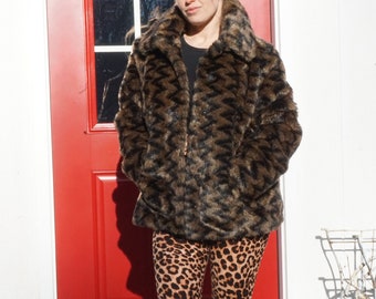 May include: A woman wearing a brown and black faux fur jacket with a chevron pattern and leopard print leggings. She is standing in front of a red door.
