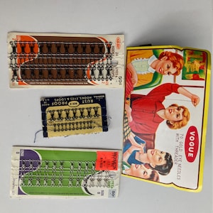 May include: Three packages of metal hooks and eyes for sewing. The packages are labeled "Rust Proof", "Rose's", and "Vogue". The Vogue package features a yellow background with three women and the text "70 Gold Eye Needles with Threader".