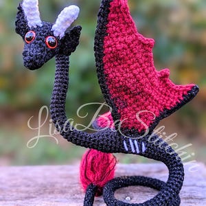 May include: A black and dark red crocheted dragon figurine with two light purple horns and bright orange eyes. The dragon has a long neck, a curled tail, and wings with a dark red interior. The text Lisa B Stitchin is overlaid on the image.