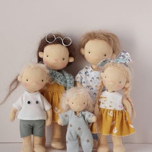 May include: Five handmade cloth dolls with different hairstyles and clothing. The dolls are wearing a variety of outfits, including a blue and white striped dress, a yellow dress with a floral pattern, a white shirt with a blue and white pattern, a blue and white striped shirt, and a blue and white striped shirt with a star pattern.